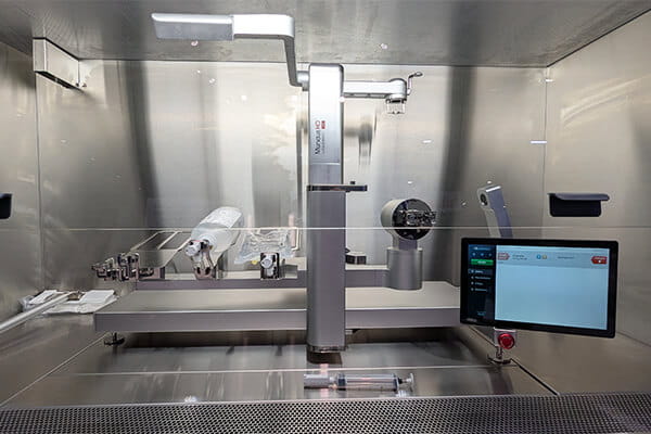 interior of a stainless steel C-PEC biosafety cabinet housing an automated hazardous drug compounding device with integrated touch screen and robotic arm system
