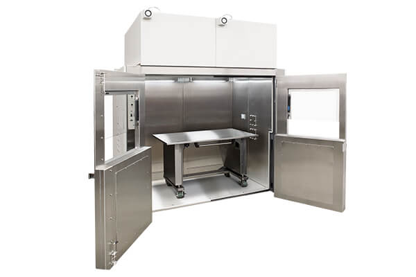 room-sized biosafety cabinet with open double doors and a stainless steel table on casters inside, designed to enclose large robotic systems for safe containment and airflow control