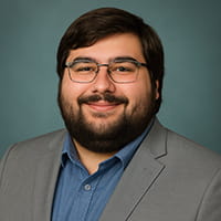 Damian Kurtz, Custom Products Sales at NuAire, professional headshot in gray blazer and blue shirt, smiling with glasses and beard.