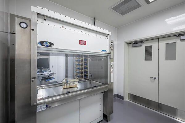 wall-mounted biosafety cabinet pass-through in a vivarium facility, shown with a small animal cage inside and cleanroom doors adjacent, designed for safe animal transfer between rooms 